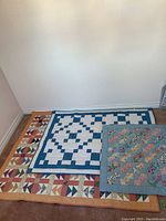 Three geometric quilts laid on floor in front of wall showing size and pattern differentiation.