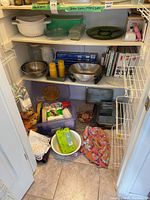 Metal mixing bowls, yellow plastic tumblers, kitchen books, baking pans, and kitchen linens in cabinet and on floor.