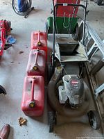 Craftsman gas lawn mower with Briggs & Stratton engine alongside three red jerry cans and Scotts fertilizer spreader