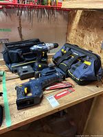 Photo of drill, reciprocating saw, tool bags, batteries, charger on a workbench