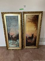 Both framed elk paintings leaning side by side against wall on carpeted floor