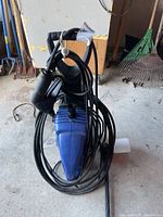 Overall view of the blue Simoniz electric power washer with hose coiled around and the attached spray gun hanging over the unit.