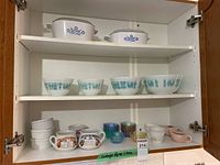 Two white CorningWare casserole dishes with blue floral patterns and clear glass lids on upper cabinet shelf.