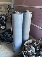 Two standing large rolls of roofing material with gray plastic backing visible on the outside and compactly rolled with a cardboard core inside.