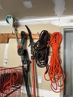 Photo showing tree pruner, saw on pole, and bundles of rope hung on wall