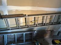 Two aluminum extension ladders, one longer and one shorter, hanging on wall with a wooden platform beneath them.