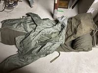 Image showing men's XL olive green rain and wind shield coat and pants laid out with sleeping robe and canvas bag.