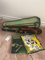 Violin in open green-lined hard case with two bows and two sheet music books in front