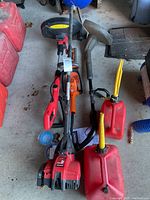 Photo showing two gas weed edgers/trimmers laid on concrete floor with two red plastic jerry cans beside them.