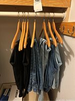 Six pairs of jeans hanging on wooden hangers on a closet rod, showing various blue jeans and one black pair.