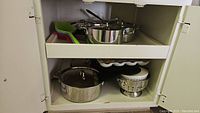 Two-shelf cabinet containing cookware, serving pieces and utensils