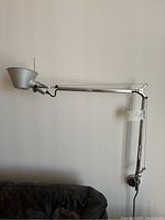 Side view of the Artemide Tolomeo lamp showing the full length adjustable arm, silver-tone cone-shaped shade, and wall mounting base.