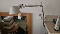 Side view of adjustable arm desk lamp clamped to table edge, showing silver metal arm, shade, and clamp base.