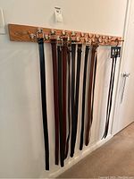 Wide shot of nine leather belts hanging on a wall rack with hooks, showing the range of colors from black to various shades of brown.