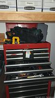 Overall view of red tool chest with ten drawers, black Craftsman tool bag on top and yellow saw handle