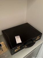 Closed briefcase showing black leather exterior, handle and gold-tone locks