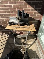 Front view of the miter saw mounted on the foldable worktable against a brick wall in sunlight.