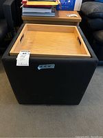 Full view of the black leather ottoman cube with wooden tray top removed showing interior storage space; tray is light natural wood with handles on both sides.