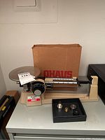 Ohaus Dial-O-Gram 2610 scale alongside box, weights set in tray and plastic scoop.