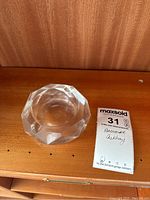 Photo of the faceted crystal ashtray placed on a wooden surface with a MaxSold lot tag; shows shape and size reference.