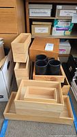 Photo showing multiple wooden file boxes and stacking organizers, natural wood finish, arranged in stacks and groups near shelves.