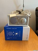 Tivoli Model One BT radio on its original box with power cord coiled on top, displayed on wooden table.