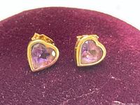 Front-facing view of both heart-shaped amethyst stud earrings on burgundy background