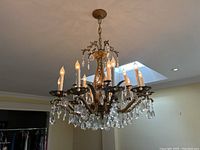 Full view of chandelier hanging in room, all ten arms illuminated with crystals visible