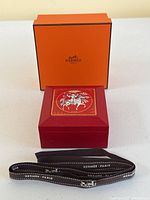 Red enamel box with lid, orange outer box, and black ribbon displayed front