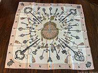 Full square view of pink and cream scarf with key motif spread flat on surface