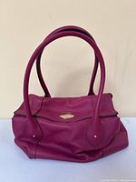 Front view of magenta leather handbag showing fold-over flap and gold-tone turn-lock