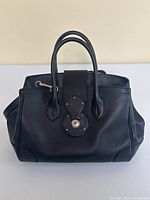 Front view of black leather handbag showing strap closure and handles
