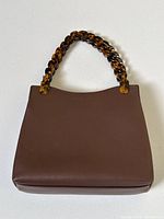 Overall front view of structured brown leather handbag with tortoiseshell acetate link handle