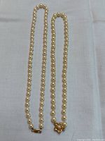 Full-length view of both pearl necklaces laid side by side on fabric surface