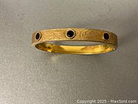 Front view of gold-filled bangle showing three round purple amethysts and foliate engraving