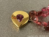 Close-up of gold heart-shaped clasp with flush-set pear-shaped pink tourmaline