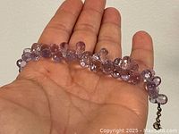 Bracelet held in hand showing faceted amethyst beads and lobster clasp