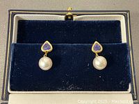 Pair of heart-shaped tanzanite stud earrings with pearl drops displayed in navy velvet box