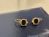 Front view of both earrings on dark blue surface showing black onyx in gold setting