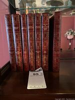 Seven hardcover books with maroon covers and gold embossed spines lined on a wooden surface.