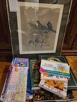 Photo shows framed bird print with image of two birds perched on a branch, stack of assorted bird watching and gardening books, and several folded maps including a Georgia map.