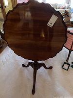 Table shown upright with top tilted and supported by pedestal base and legs, showing scalloped edge and polished wood surface.