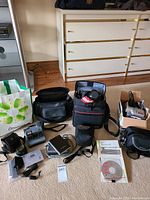 Front view of Canon and generic camera bags, Canon SLR camera inside Canon bag, Polaroid camera on floor, iNEO drive, Sony device, instructional CD