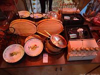 Photo of entire lot showing two wooden cheeseboards, five copper pans including one with lid, six cocktail-themed ceramic plates, 24 spice jars in black boxes, French press and metal coffee cup.