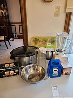 Lot layout showing Crock Pot, blender with coffee grinder, chopper box, cutting board, sieve, cheese grater, juice jug, butter warmer