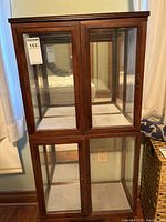 Front view of the wood framed glass display case with two doors on upper and lower sections and a mirror on the back interior panel.