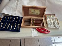 Group shot: six steak knives in wood box, tray of cat-shaped utensil rests, tray of escargot forks and red lobster tool