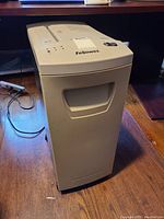 Shredder full view showing body, control panel, and power cord on wooden floor.