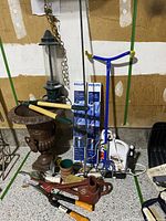 Full overview of the garden lot items including urn, bird feeder, Philips lawn stakes, branch trimmer, watering can, Roundup bottle, garden tools, and flower pots.