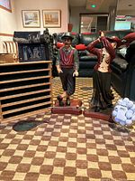 Two large golf figurines, male and female, standing upright on wooden bases with a large clear wine glass filled with golf balls and the wooden golf ball display case behind them.